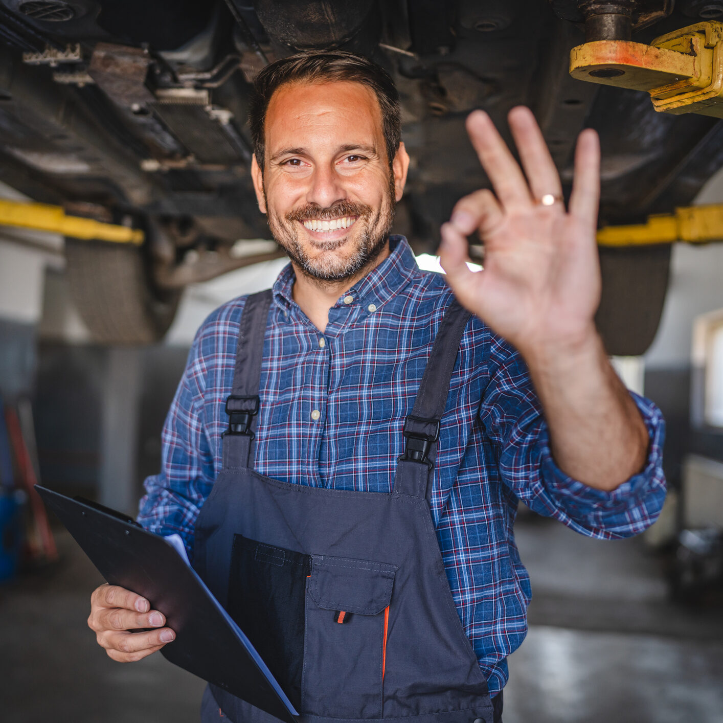 Car mechanic making gesture under the car with friendly smile Car mechanic making okay gesture under the car with friendly smile